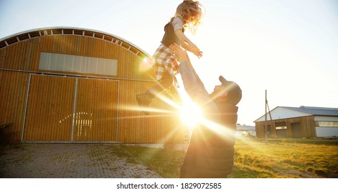 Caucasian young handsome father playing with small cute daughter and tossing up in air. Outdoor in sunlight. Farming lifestyle. Man having fun and throwing up kid at farm. Summer at countrysie.