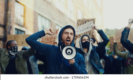 Caucasian young handsome guy protesting in middle of multiethnic crowd of protesters and screaming mottos in megaphone. Guy leading at manifestation for human rights. - Powered by Shutterstock