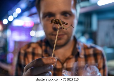 Caucasian young male eating cricket at night market in Thailand. Eating insect concept