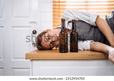 Caucasian young male lying on dining counter after drink beer at home. Attractive handsome man with a bottle of alcohol, feel drunk and hangover alone in kitchen in house then sleeping on eating table
