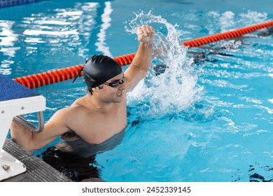 Caucasian young male swimmer celebrating indoors in pool, splashing water. He has short dark hair, wearing swim cap and goggles, looking fit, unaltered. - Powered by Shutterstock