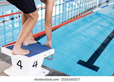 Caucasian young male swimmer preparing to dive into an indoor pool. He has short brown hair, wearing dark swimsuit, focused on his training, unaltered. - Powered by Shutterstock