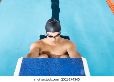 Caucasian young male swimmer preparing to dive into indoor swimming pool. Wearing goggles, short brown hair showing, focusing on training, unaltered - Powered by Shutterstock