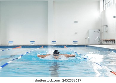 Caucasian young male swimmer training indoors in an indoor pool, wearing goggles, copy space. He has short dark hair, a fit body, and is focused on his swim, unaltered - Powered by Shutterstock