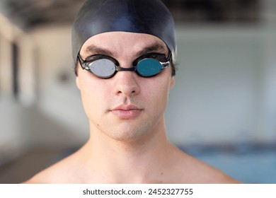 Caucasian young male swimmer wearing goggles and cap is ready to swim indoors. He has short hair, fair skin, and is wearing dark swimwear, unaltered. - Powered by Shutterstock