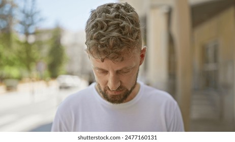 Caucasian young man with blue eyes and beard looks down pensively on a city street. - Powered by Shutterstock