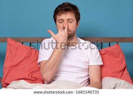 Caucasian young man breathing Alternate Nostril Breathing exercise, nadi shodhana pranayama, working outsitting in bed during quarantine. Stay calm, stay home concept.
