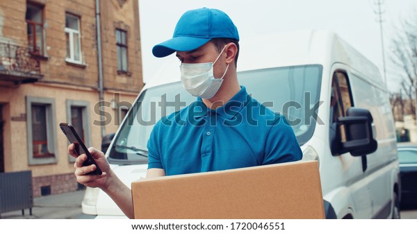 Caucasian young\
man, delivery worker in cap carrying carton box and tapping on\
smartphone. Male courier with parcel texting or scrolling on phone.\
delivery bus background.\
Outdoor.