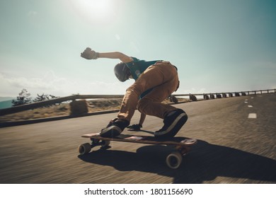 Caucasian young man drifting his longboard on extreme asphalt slope in a very sunny day