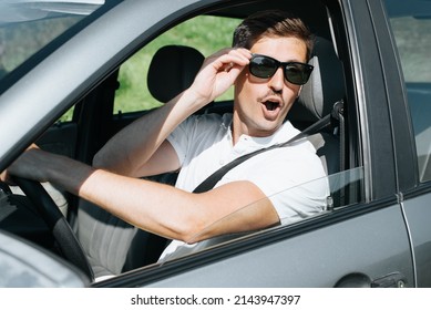 Caucasian Young Man Driving Car With Surprised, Shocked Expression And Open Mouth Looking Away At Something. Handsome Guy Driver In Wow Effect Sitting Behind Wheel. Incident, Incredible Event Concept.