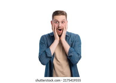 Caucasian Young Man With Dropped Jaw And Wide Opened Eyes Posing In Bright Studio. Shocked Male Person Holding Hands On Cheeks And Expressing Surprisement.