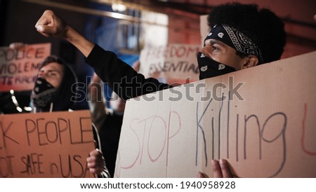 Caucasian young man in hood standing in crowd of people at street protest with poster No racism at night. USA manifestation for equal human rights. Male protester. Activist and leader.