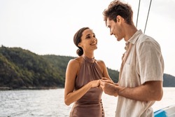 Caucasian Young Man Make Surprise Proposal Of Marriage To Girlfriend. Attractive Romantic Male Proposing To Beautiful Happy Woman With Wedding Ring Enjoying Surprise Engagement While Yachting Together