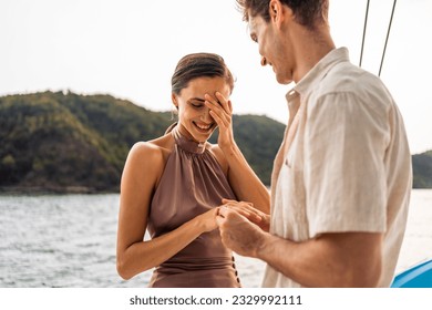 Caucasian young man make surprise proposal of marriage to girlfriend. Attractive romantic male proposing to beautiful happy woman with wedding ring enjoying surprise engagement while yachting together - Powered by Shutterstock