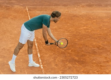 A caucasian young man in serve position on a clay tennis court. - Powered by Shutterstock