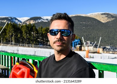 Caucasian Young Man With Sunglasses, Piercings And Black Sweater, Sitting Sunbathing In The Snow