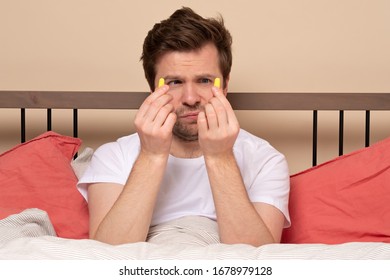 Caucasian Young Stressed Man Holding A Yellow Earplug Trying To Sleep Having Insomnia. Studio Shot