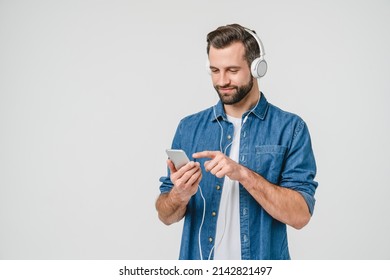 Caucasian young student man freelancer listening to the music in headphones, choosing sound track, song, playlist, podcast on phone isolated in white background - Shutterstock ID 2142821497