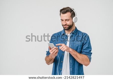 Caucasian young student man freelancer listening to the music in headphones, choosing sound track, song, playlist, podcast on phone isolated in white background
