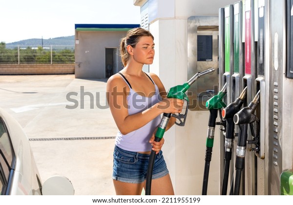 Caucasian young woman using nozzle to refuel her\
car in gas station.