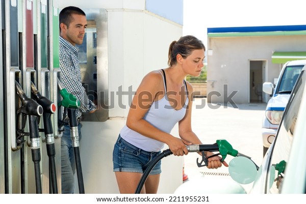 Caucasian young woman using nozzle to refuel her\
car in gas station.