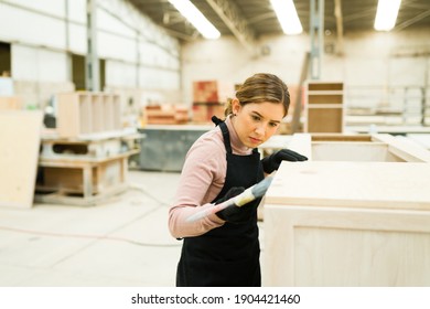 Caucasian Young Woman Wearing An Apron And Using A Paintbrush To Paint A Wood Kitchen Cabinet On A Woodshop