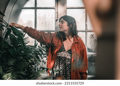 caucasian young woman wearing nice earrings red jacket calm and relaxed caressing the soft leaves of a nice plant in the botanic garden, botanic garden christchurch, new zealand - Shutterstock ID 2311555729