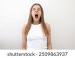 Caucasian young woman yawning and covering wide open mouth with hand isolated on white background. Girl looking sleepy and tired, exhausted for fatigue and hangover, lazy eyes in the morning