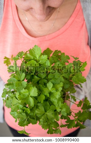 Caucasina woman wearing a salmon colored shirt holding a bunch of coriander leaves in her hand looking down.