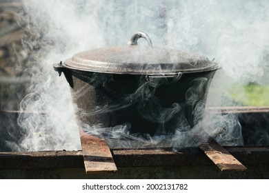 Cauldron Over Bonfire Shrouded In Smoke. Cooking Food Outdoor On Fire In Metal Pot.