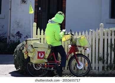 Caulfield South, Victoria, Australia - October 7 2021: An Australia Post Postie On A Bike Outside A House, In Standard Fluorescent Protective Gear, Sorting Letters.