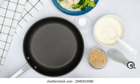 Cauliflower And Broccoli Casserole Recipe. Frying Pan, Vegetables, Alfredo Sauce, And Bread Crumbs Close Up On Kitchen Table, Flat Lay