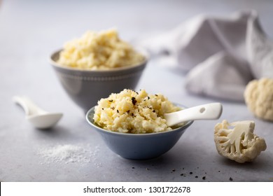 Cauliflower Mash Served In Grey Bowls With Cauliflower Florets And Linen Napkin On Pale Grey Worktop