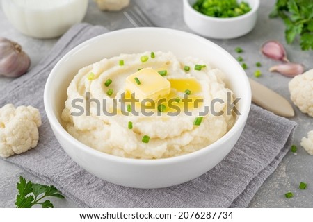 Cauliflower puree with butter and green onions in a white bowl on a gray concrete background. Healthy food. Copy space