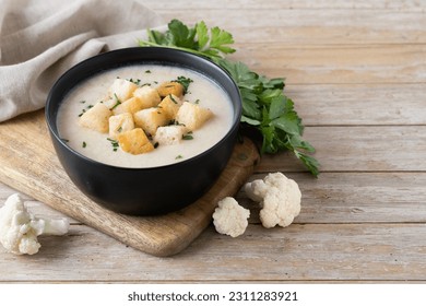 Cauliflower soup in a bowl on wooden table. Copy space - Shutterstock ID 2311283921