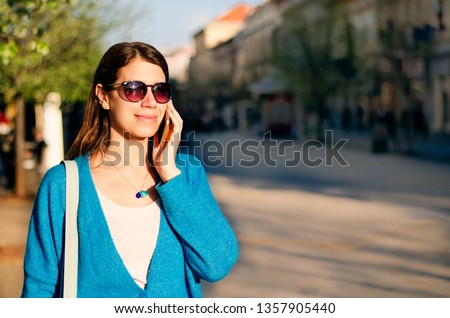 Causal young woman walking through the town at sunset having sunglasses on and making a phone call. 