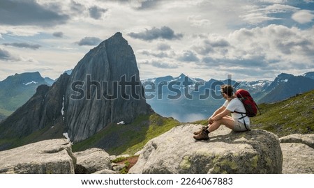 Causasian hiker sitting down on a rock on Hesten mountain looking to Segla mountain, Senja island, Norway