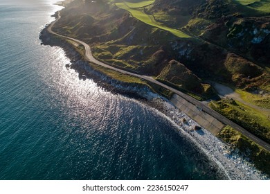 Causeway Coastal Route a.k.a Antrim Coast Road A2 on the Atlantic coast in Northern Ireland. One of the most scenic coastal roads in Europe. Aerial view against the rising sun in winter - Powered by Shutterstock