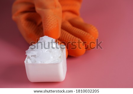 Caustic soda flakes are placed in a spoon and there is a hand holding a spoon.