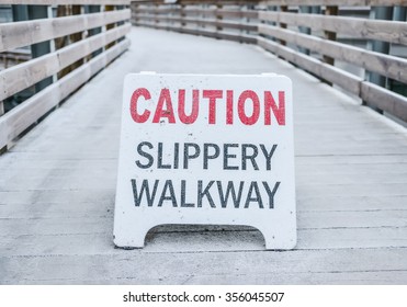 Caution Slippery Walkway Warning Sign On The Walk Way Cover With The Ice In The Park.