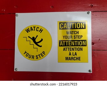 A Caution Watch Your Step Sign Attached To A Red Wall.