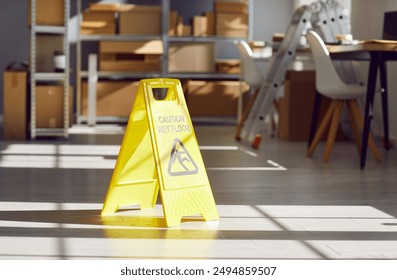 Caution Wet Floor sign left by janitorial service workers in sunlit warehouse storage room. Yellow warning sign with falling human pictogram on clean slippery floor, with blurred shelves in background - Powered by Shutterstock