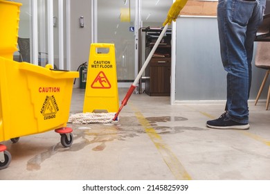 A Caution Wet Floor sign placed to warn passersby while wiping a wet concrete floor with a string mop. - Shutterstock ID 2145825939