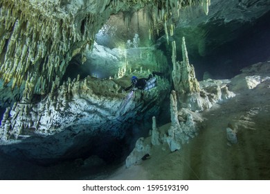 A cave diver swims in the Hulo cenote (Mexico), illuminated by the AMG's underwater light. Karst cave, formed stalactites and stalagmites are visible.