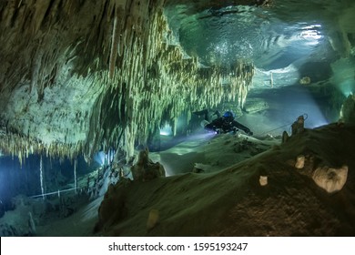 A cave diver swims in the Hulo cenote (Mexico), illuminated by the AMG's underwater light. Karst cave, formed stalactites and stalagmites are visible.