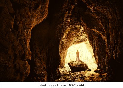Cave with man standing on a rock in front of the entrance with trees behind him