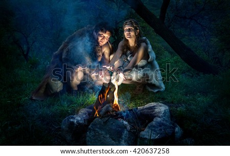 Cave people dressed in animal roast oneself at bonfire in the forest