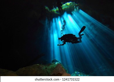 Cave technical diver swimming from the light into darkness. Scuba diver in the cenote and sun rays. Underwater photography from the cave exploration.
