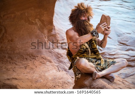 Caveman watching the screen of his primitive stone tablet outdoors in a weathered rock cave