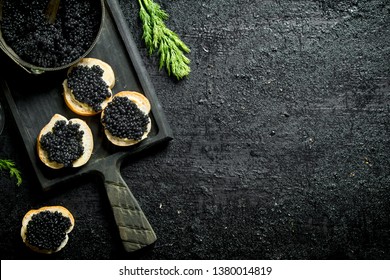 Caviar sandwiches and caviar in a bowl on a cutting Board. On black rustic background